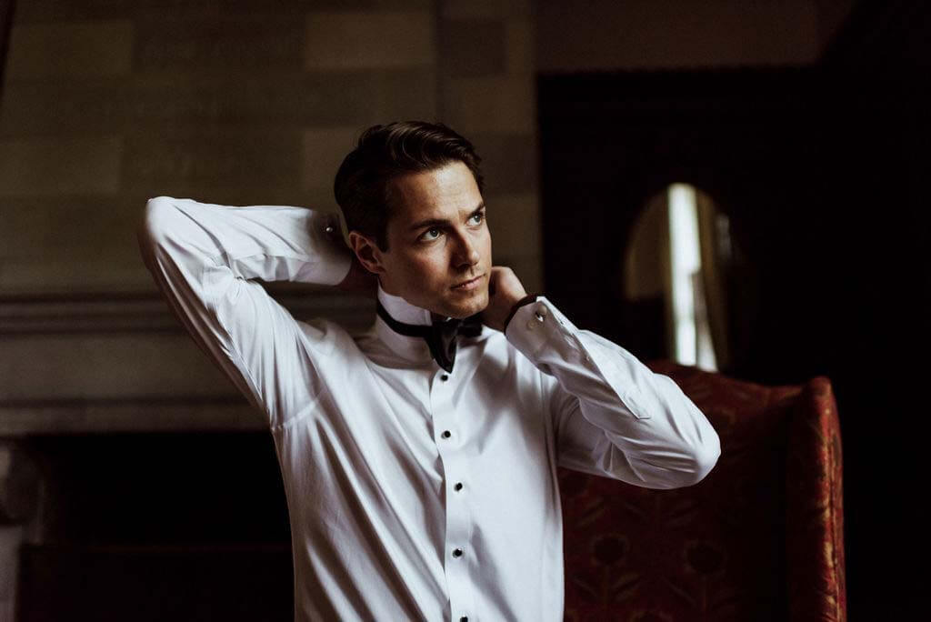 The handsome groom adjusts his bowtie while getting ready for first looks. Groom adjusts bowtie