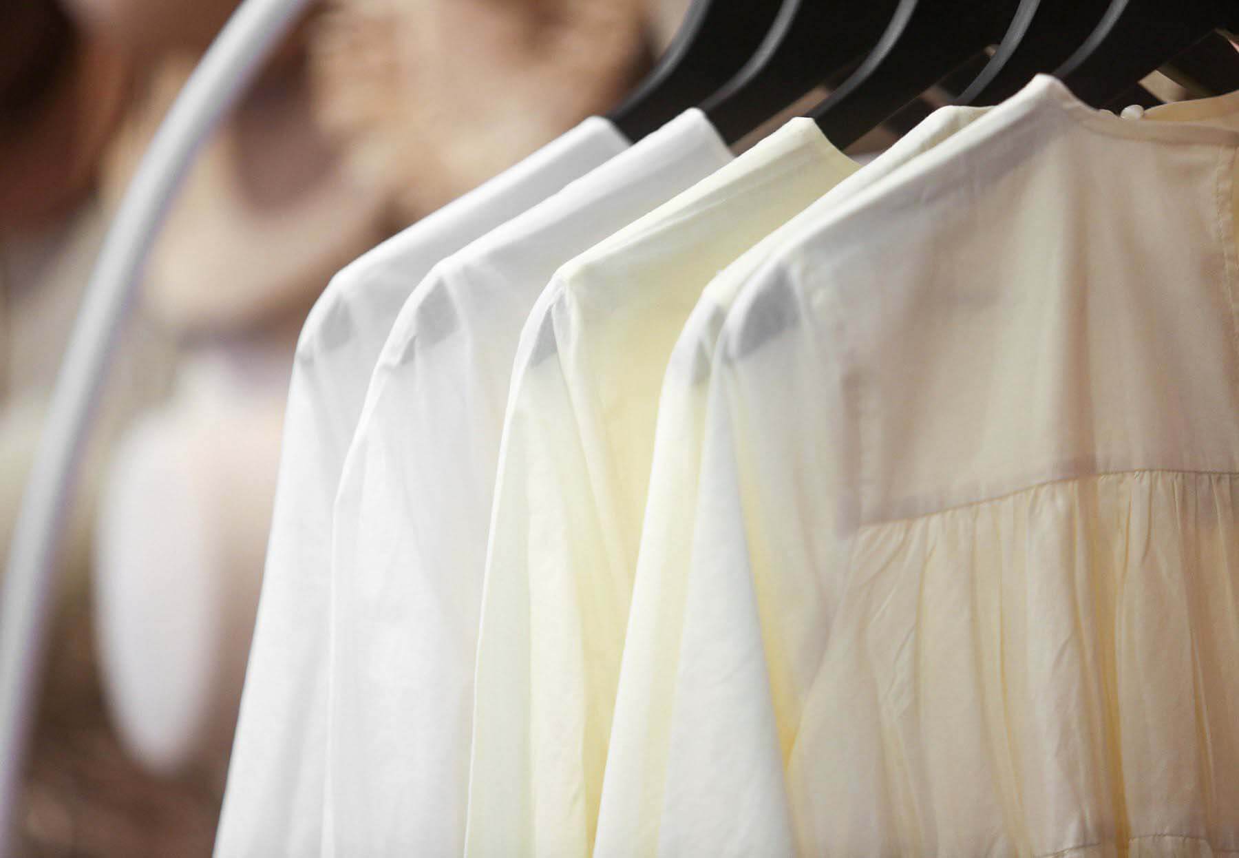 Clothing from handpicked, high-end brands are intermittently spread throughout the space. row of white blouses
