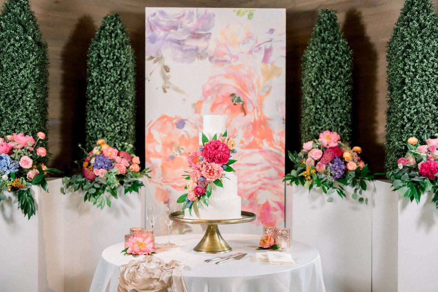 Make your cake a focal point by creating a display complete with lighting, flowers and even art. Image: Eric & Jamie Gay Photography Wedding cake surrounded by art and flower, a wedding trend in 2020