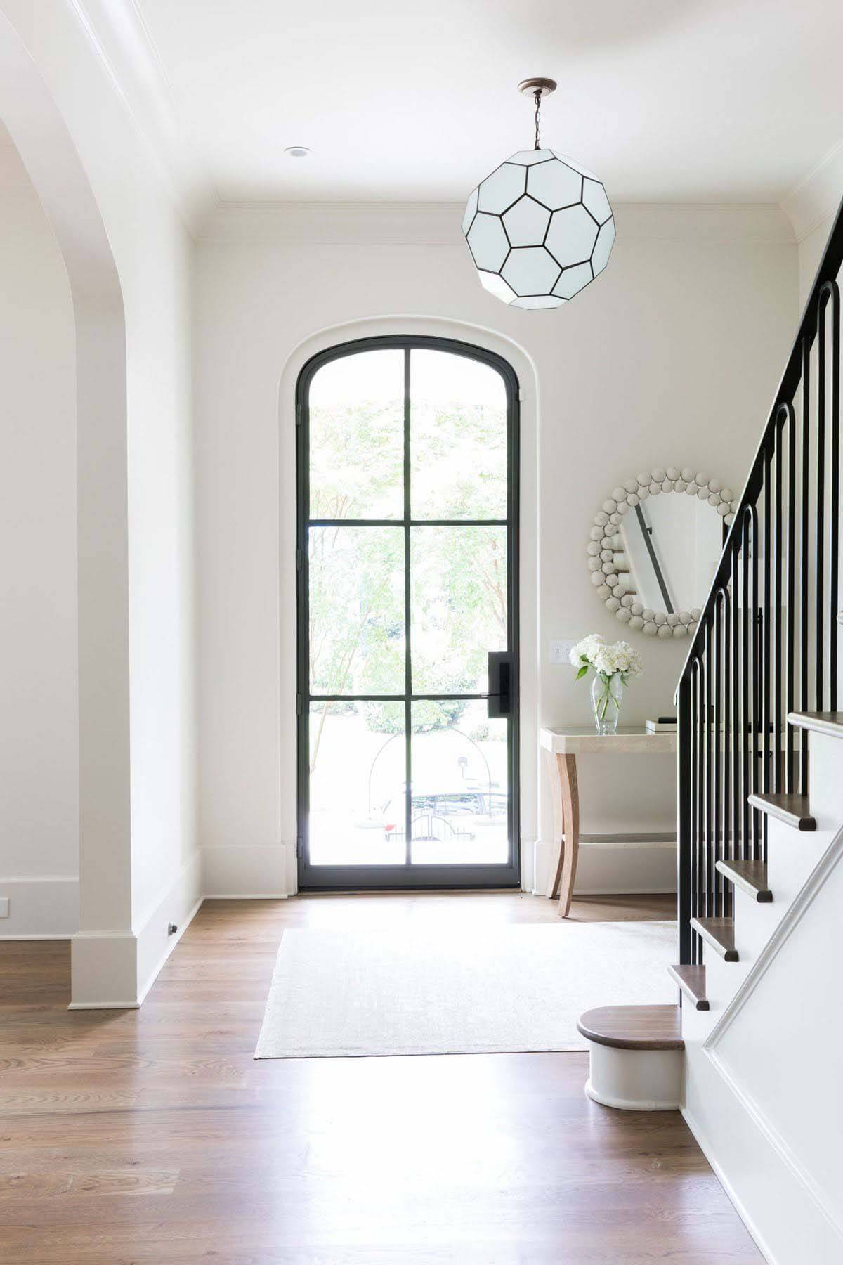 The front entry was designed with a clean-lined approach. “We wanted to keep the foyer clean and bright,” says the architect. “The charcoal-painted steel door provides the maximum amount of light possible, while remaining elegant and not too stark/industrial feeling.” Glass door in entryway in modern Atlanta home