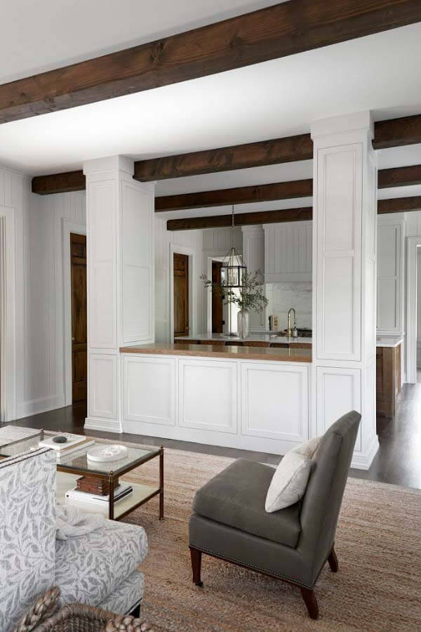 Dark wood beams create a dramatic contrast throughout the home, offering a masculine touch that juxtaposes the feminine design elements. Kitchen opening up into living room