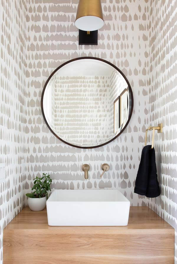A wallpaper addiction, something Sara admittedly has, means wallpaper is likely to be included in each of her designs. Here, wallpaper with an approachable pattern and color palette softens the clean lines of the small powder room and pairs well with many materials. Bathroom with patterned wallpaper