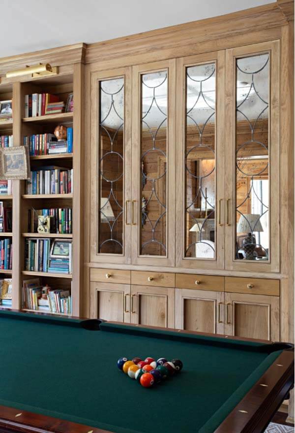 The bar's antiqued mirror doors can be closed for a clean, elegant look. Image: Caroline Sharpnack A billiard table in front of the bar with vintage glass windows — an inspired room