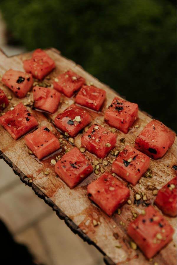 Watermelon squares served on a rustic wood plank and topped with pistachio crumbles make for a mouthwatering and dazzling starter during cocktail hour. Watermelon appetizer during cocktail hour