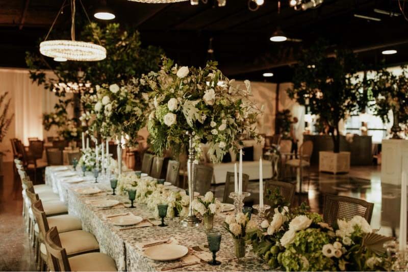 H Three Events designer Hugh says, "We selected lush linens and transformed the entire event center into a garden — complete with life-size trees, custom bars, and hand sanitizing stations. In fact, the escort cards were personalized hand sanitizer bottles." French country-themed reception tables lined with dinnerware and flowers