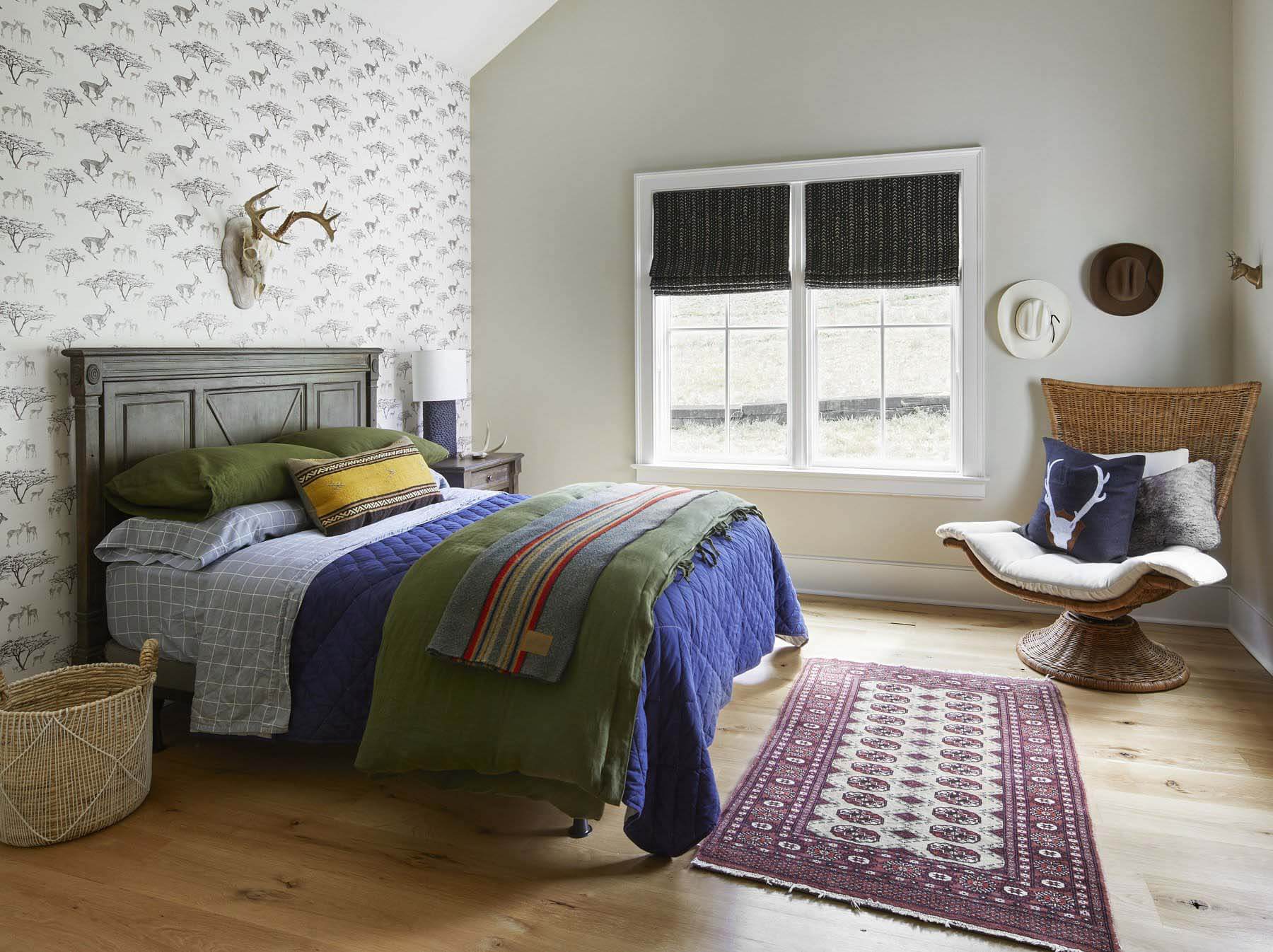 The middle child, who shares his father's love for hunting, opted for an antelope wallpaper. Again, muted colors work together to create an approachable design. Don't overlook the vintage brass deer hood on the right wall. Bedroom with antelope wallpaper and muted color scheme