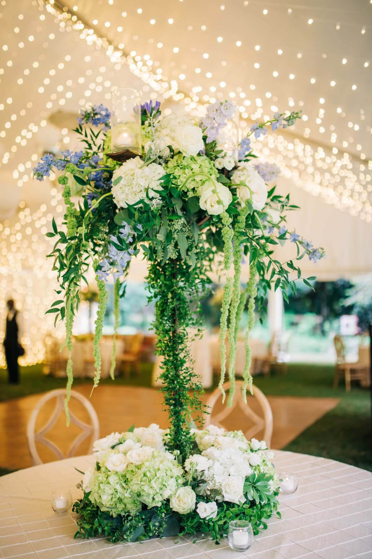 "Warner did a magnificent job with the flowers,” says Mark. “He said, ‘I'm going to show you the quote for the flowers, and I don't want you to have a heart attack; we can talk about it.’ Then I saw the quote and literally almost had a heart attack. After the wedding, this SWAT guy buddy of mine comes up to me, and he's like, 'If I notice the flowers at a wedding, you had really good flowers!'" Tall floral arrangement at Greaney wedding