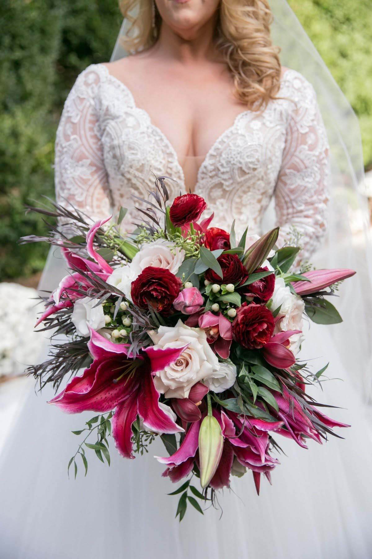 Bright burgundy florals from Lauren Atkinson Designs offer a majestic pop of color against the bride's beautiful gown. Close-up of bride's bouquet