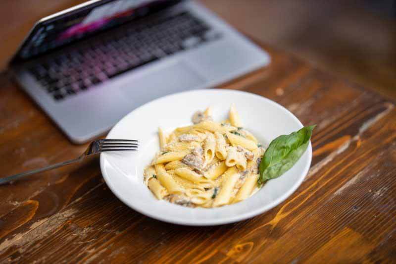 Working from home poses its share of challenges, including mindless eating in the throes of the workday. A bowl of pasta next to a laptop