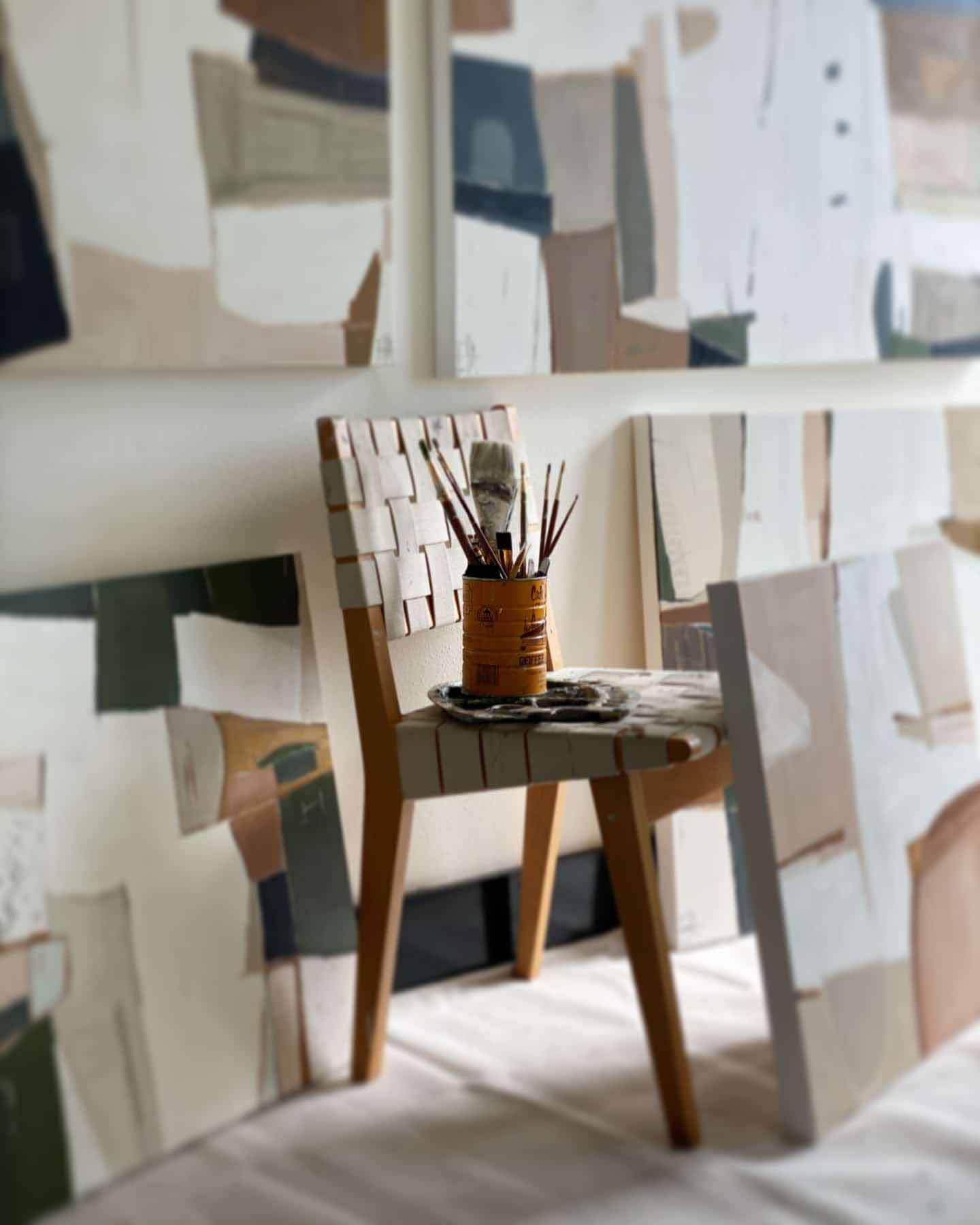 Painting supplies sitting on chair surrounded by Sarah Ella Cole paintings