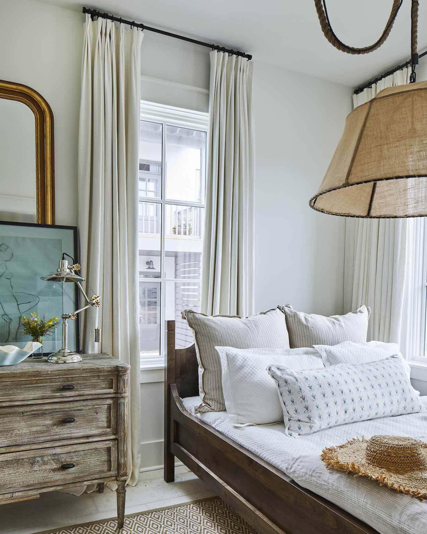 Tucked behind the dining room and kitchen, this small-but-sweet bedroom features a single full bed below a large light fixture that balances the asymmetrical layout. Bedroom in Ashley Gilbreath's Rosemary Beach house