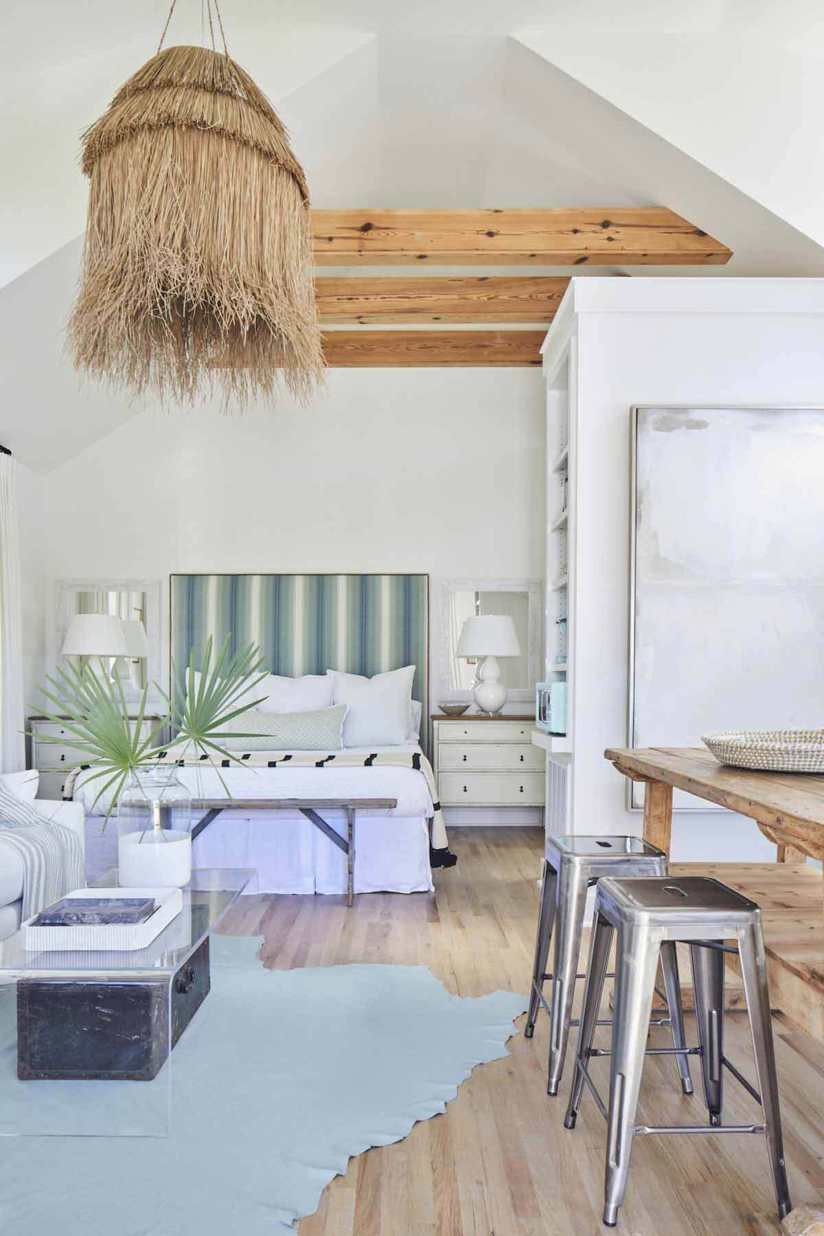 The design details found inside the main house extend into this space, which has a simple palette of whites, wood tones and blues. Wood beams and oak flooring were refinished to complete the design. Bedroom in carriage house of Ashley Gilbreath's Rosemary Beach house