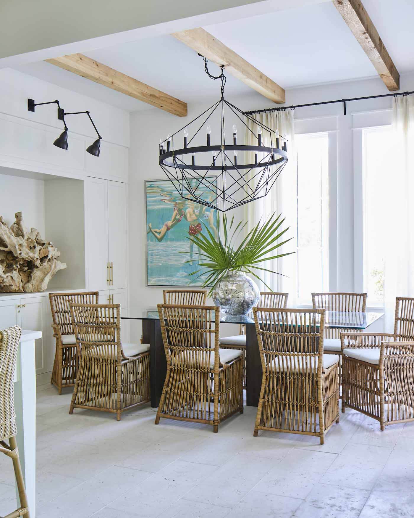 Ashley chose an oversized chandelier and a glass-top table to help the small space feel bigger, and she sourced a custom table base to fit the aesthetic. Concrete pavers from Concrete by Design run across the main floor and were a smart choice for durable flooring. Dining room with rattan chairs in Rosemary Beach house