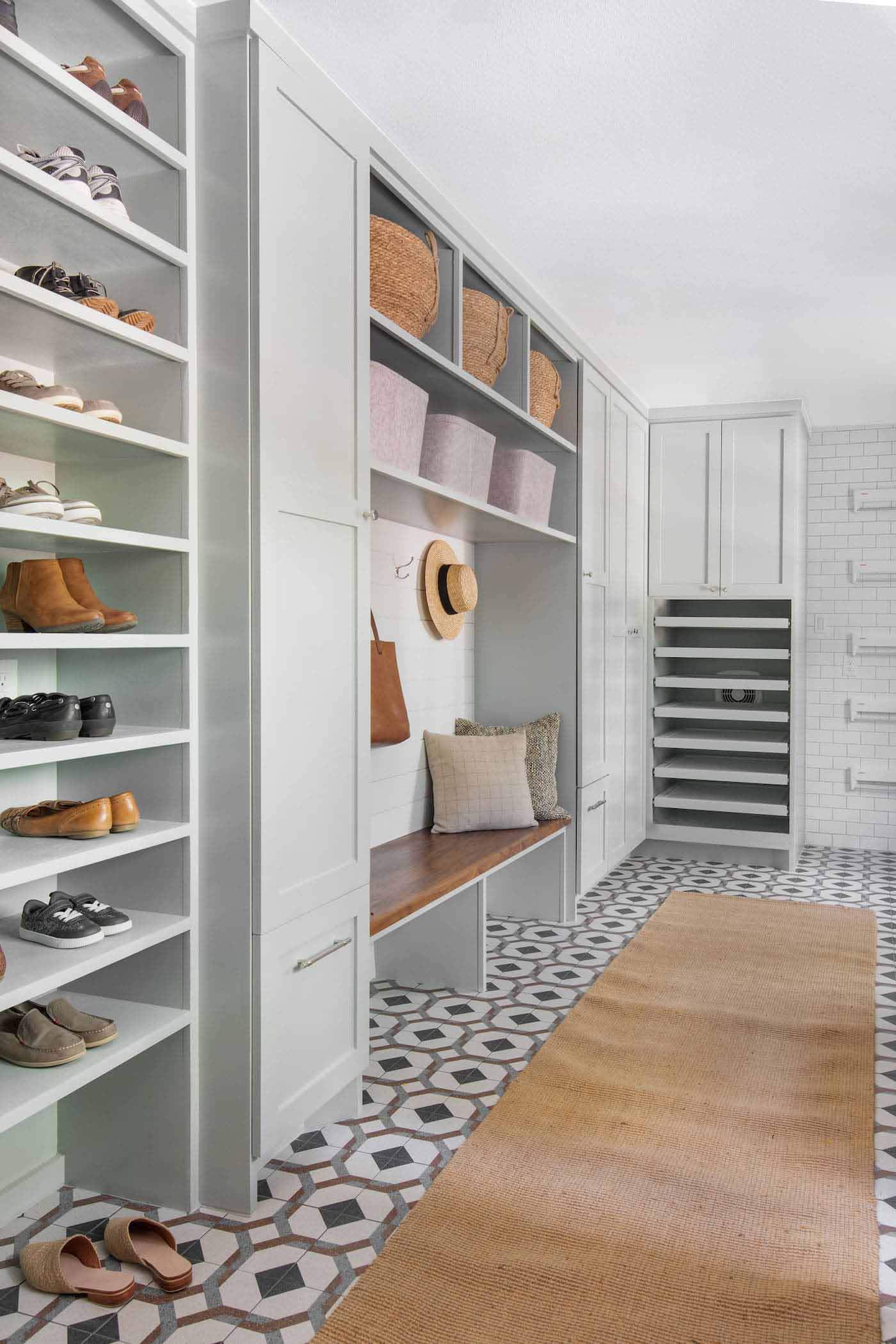 Sarah Stacey reimagined the long, narrow area to accommodate this family's unique needs. The drying racks were designed to avoid any damage to the clothes. The design includes aluminum pans to catch the water, precautions that prevent mold and mildew and an extra exhaust fan that whisks away lingering moisture. Image: Avery Nicole Photography Shelves, drying racks and bench in laundry room
