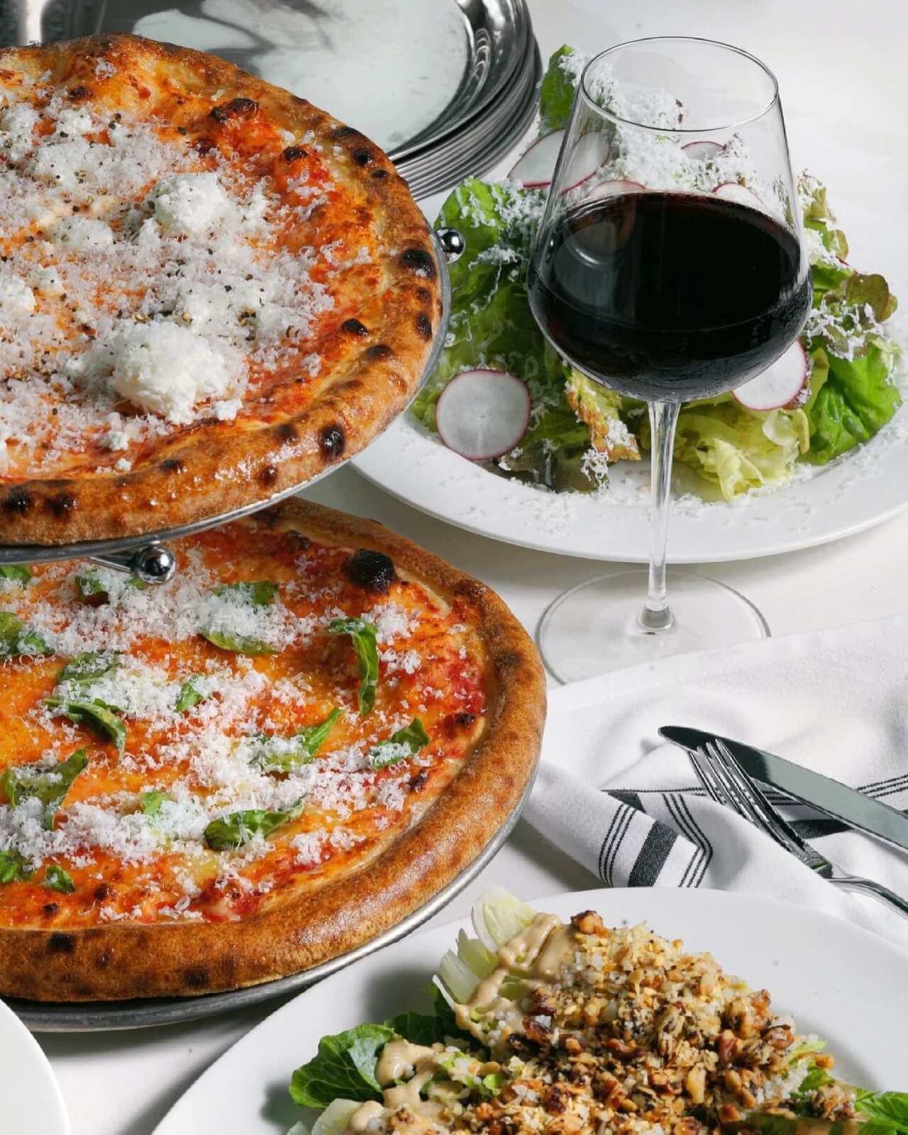Pizzas, salads, and a glass of red wine.