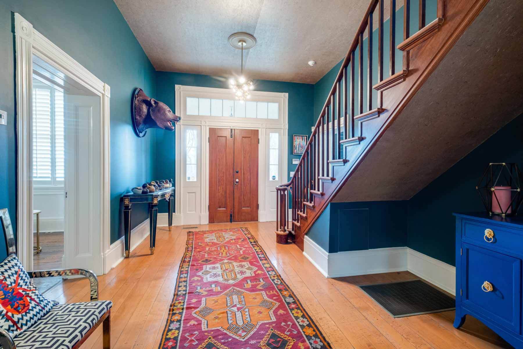 The front entryway displays the original solid-wood double doors and the home’s main staircase, which is also original to the house. The rich wall color, Evergreen from Porter's Paints, is a bold first impression. “I wanted a very dark color because I was reading something in a magazine that said when you use a darker color in an entry hall, it gives it this feeling of grandeur,” says Therese. “So, I went with super dark green. As you come in, to your right, there's a bear head — that actually came off of an old carnival ride.” Image: Zach Harrison Photography Front entryway with grand staircase. A bear head on the wall is a standout feature.