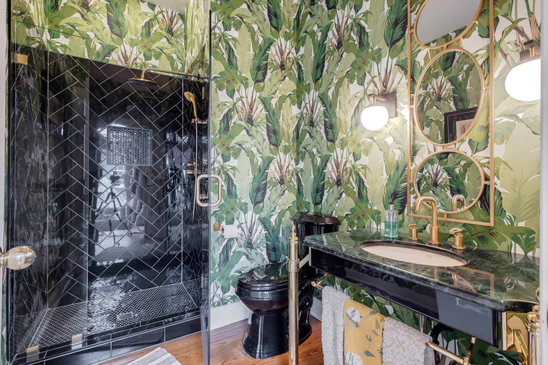 The downstairs full bath is a tropical paradise with a remake of the banana leaf wallpaper from the Beverly Hills Hotel in Los Angeles. Right off of the family room, it's a funky space that melds contemporary nuances such as herringbone-style black subway tile with older features such as the home's original vanity. Image: Zach Harrison Photography Bathroom with palm leaf wallpaper, a la the Beverly Hills Hotel