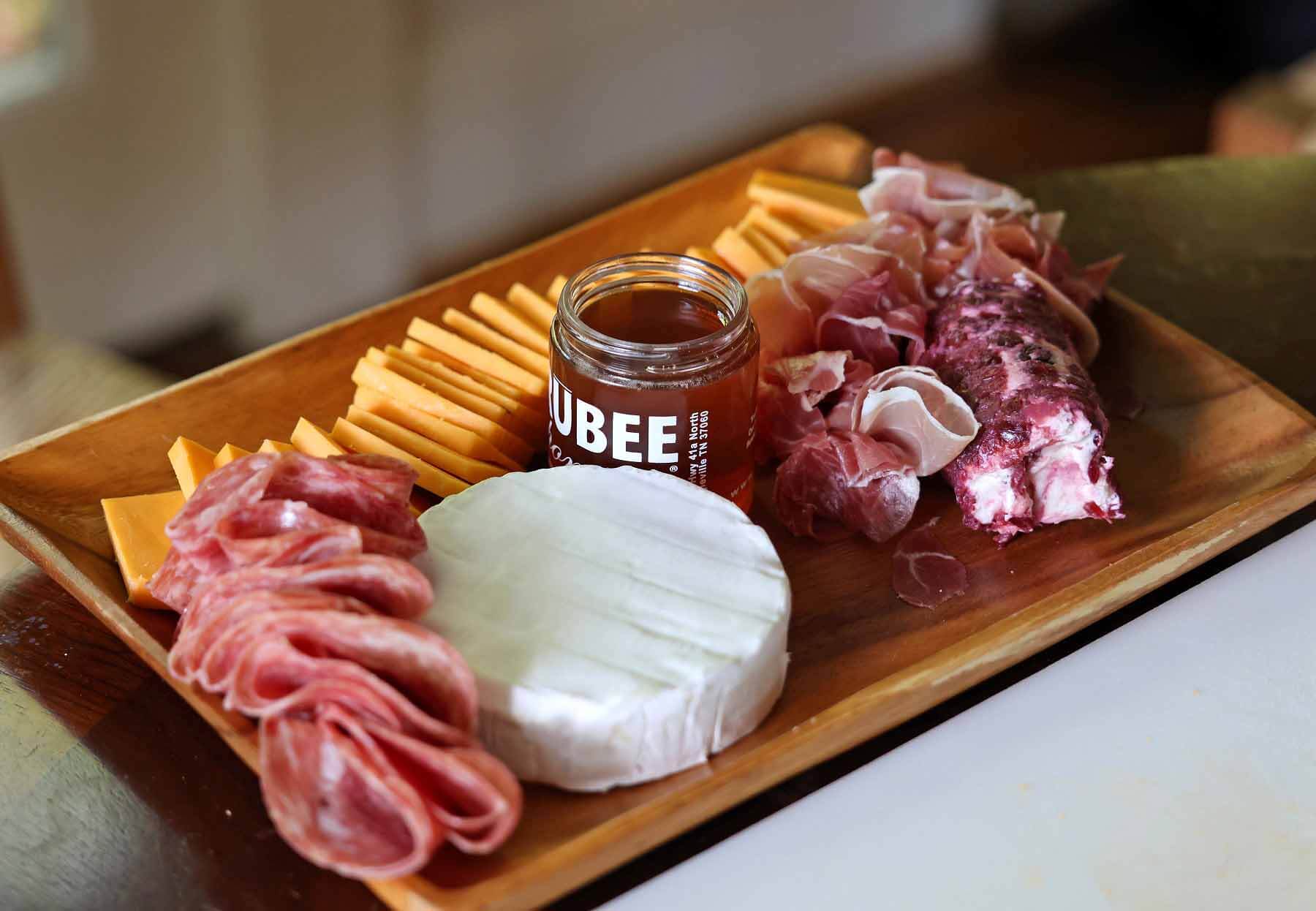 Charcuterie baord with cheddar cheese, brie cheese, soppressata, prosciutto and a jar of honey
