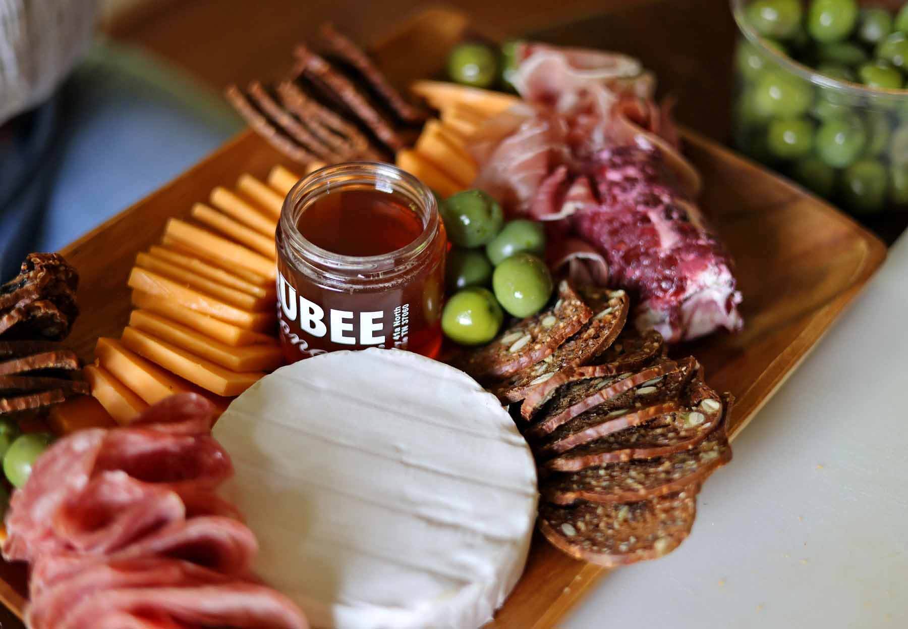 Charcuterie board that is halfway assembled with cheeses, crackers, charcuterie, and a jar of honey