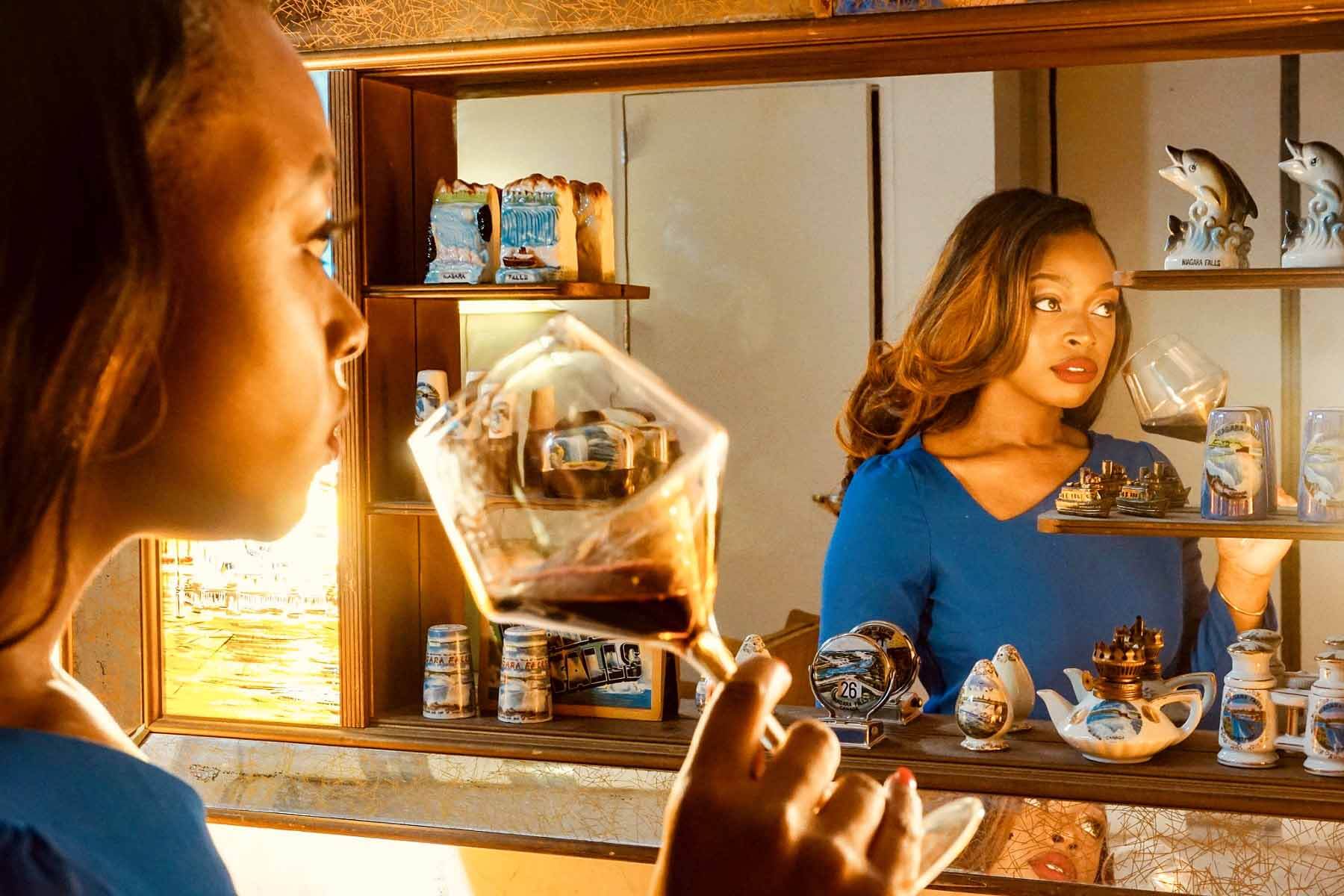 Ashley sipping from a wine glass as she looks in a mirror