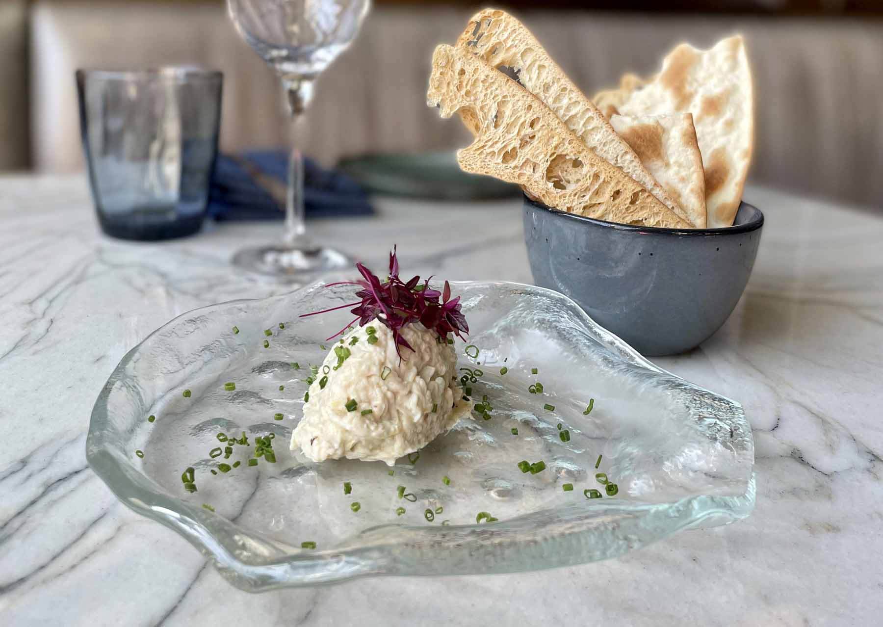 A glass platter with a scoop of smoked fish dip, accompanied by a bowl of toasted bread
