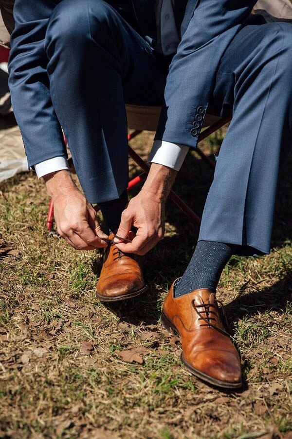 Groom Ties Shoes Before Farm Wedding