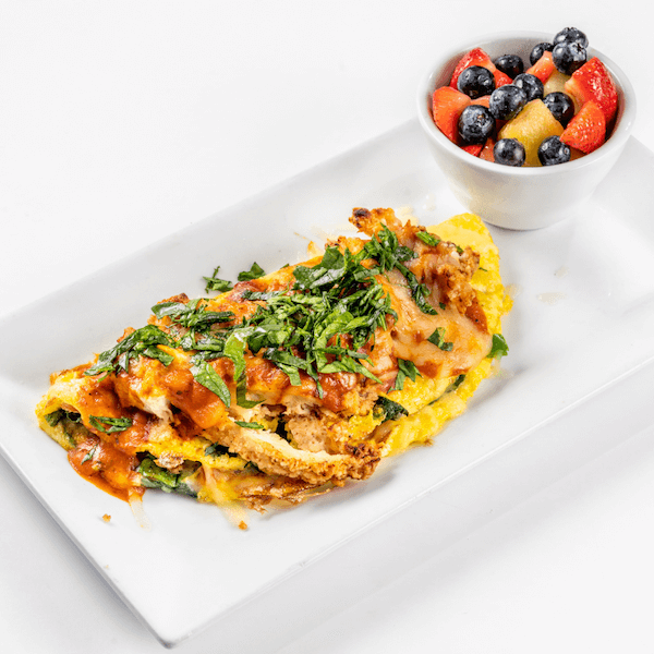 chicken parmesan omelet on a rectangular white plate with a side of fruit