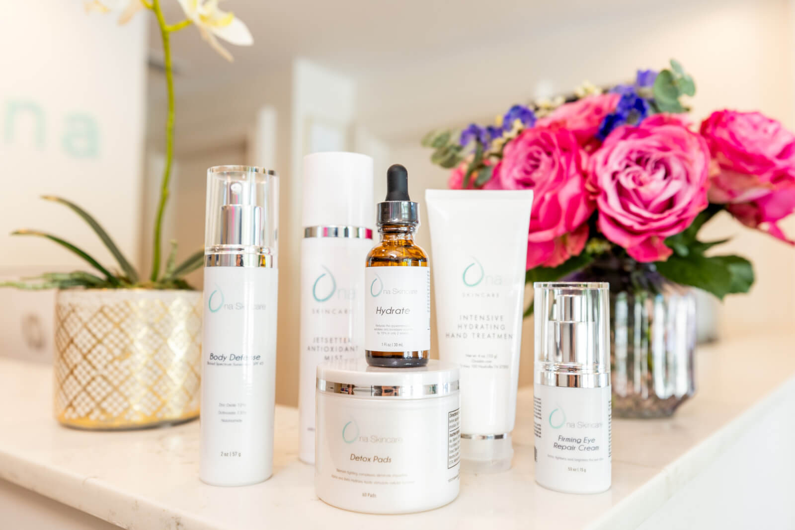 A group of white Ona Skincare containers with a dropper sit elegantly on a white surface, reflecting a clean beauty aesthetic.