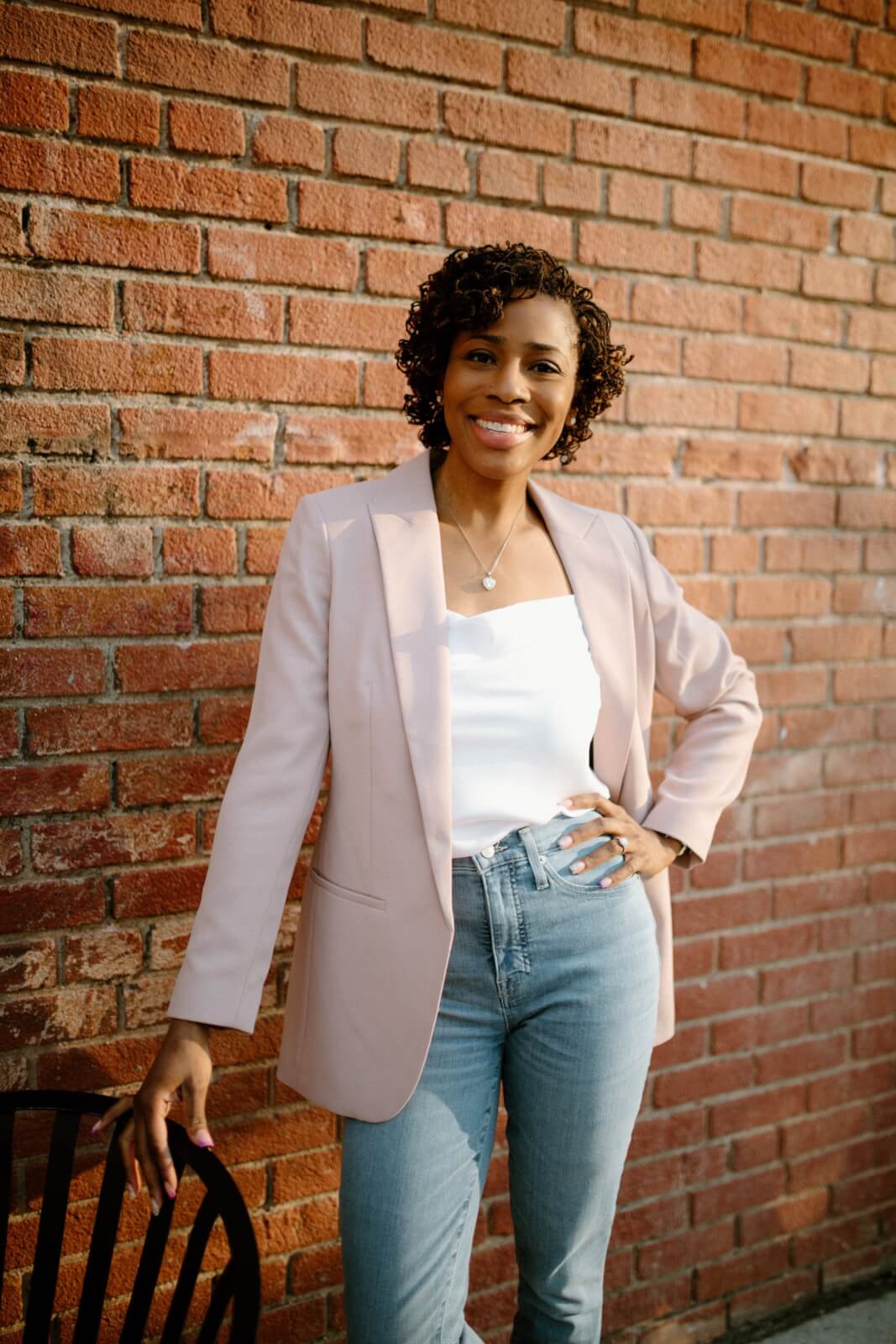 Sherilyn posing in front of a brick wall in blush blazer