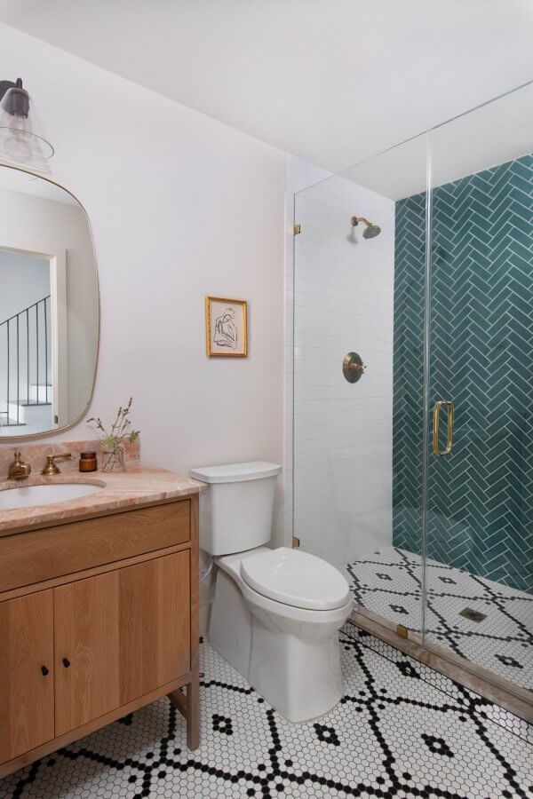 Powder room with green shower tile, pink marble sink and black and white mosaic floor.