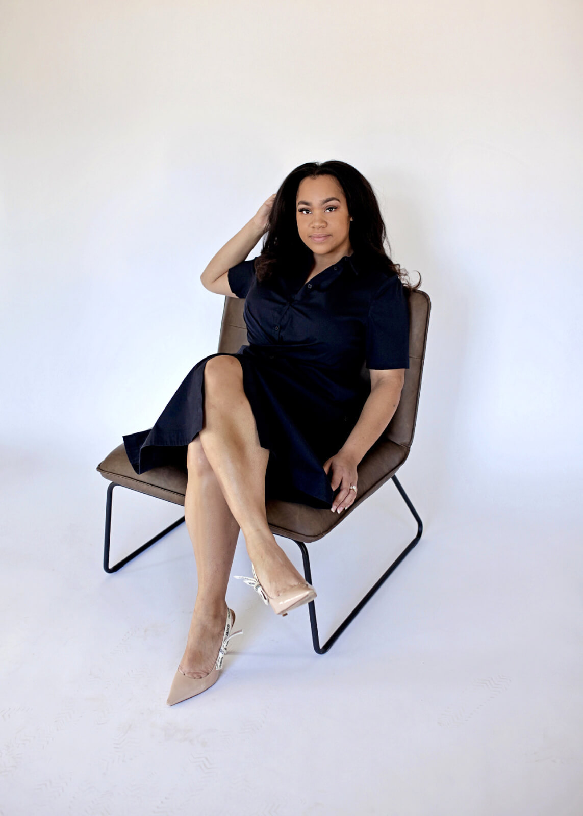 DeLisa, in a black dress, sitting in a chair against a white backdrop.
