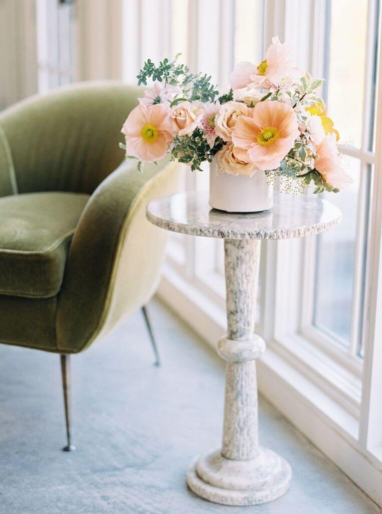 The "Lillian" arrangement by Rachel Penn, sitting on a pedestal table by a green velvet chair