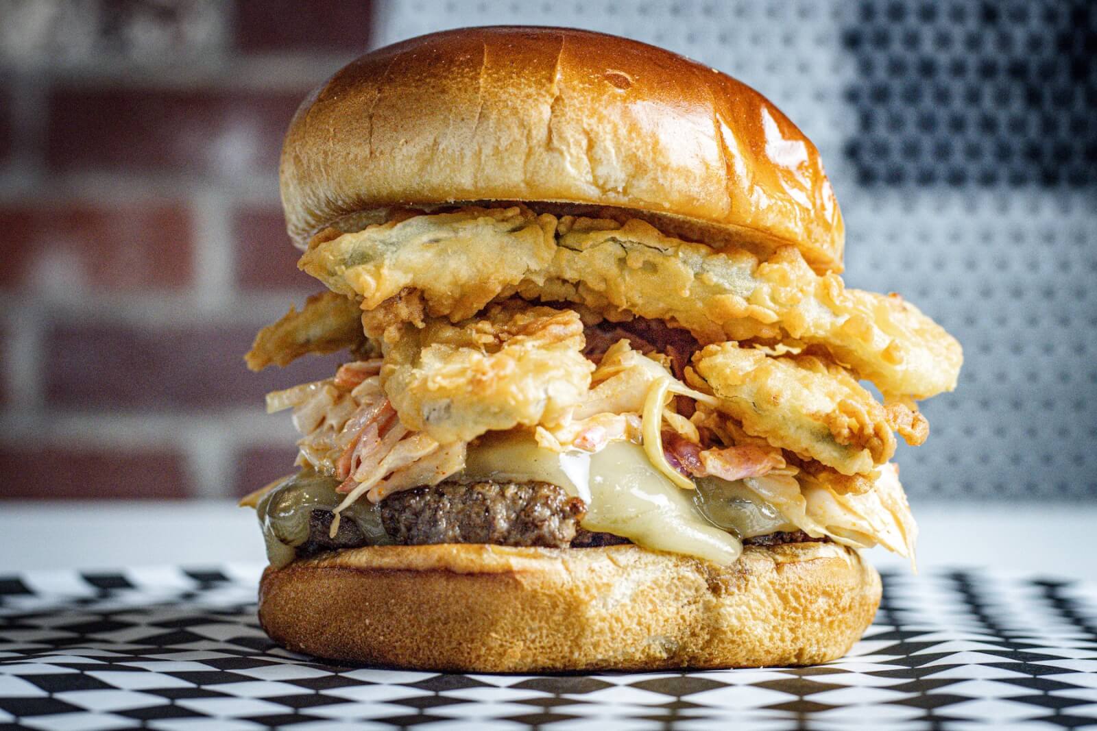 Looking for a luxe burger and fries? Grab this fried pickle burger from Burger & Company. Image: Joey Martin for WySmart Digital Luxe burger from Burger & Company on a black and white checkered paper.