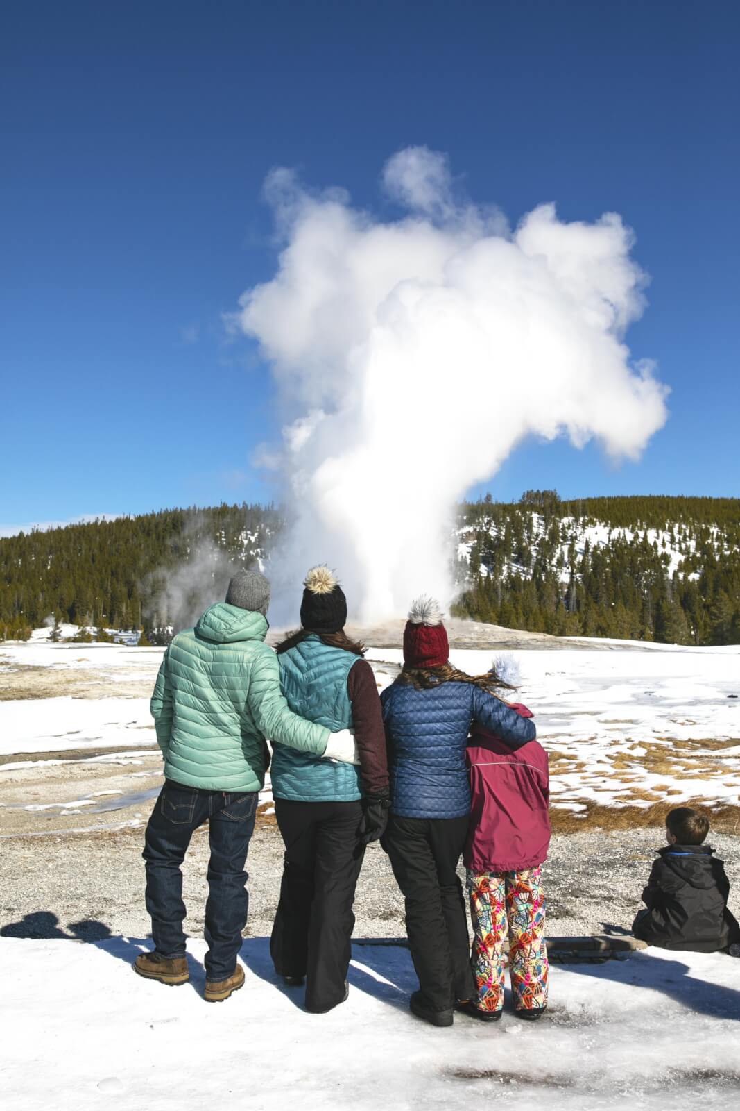 Family of four looking at steaming geyser basin in Yellowstone National Park