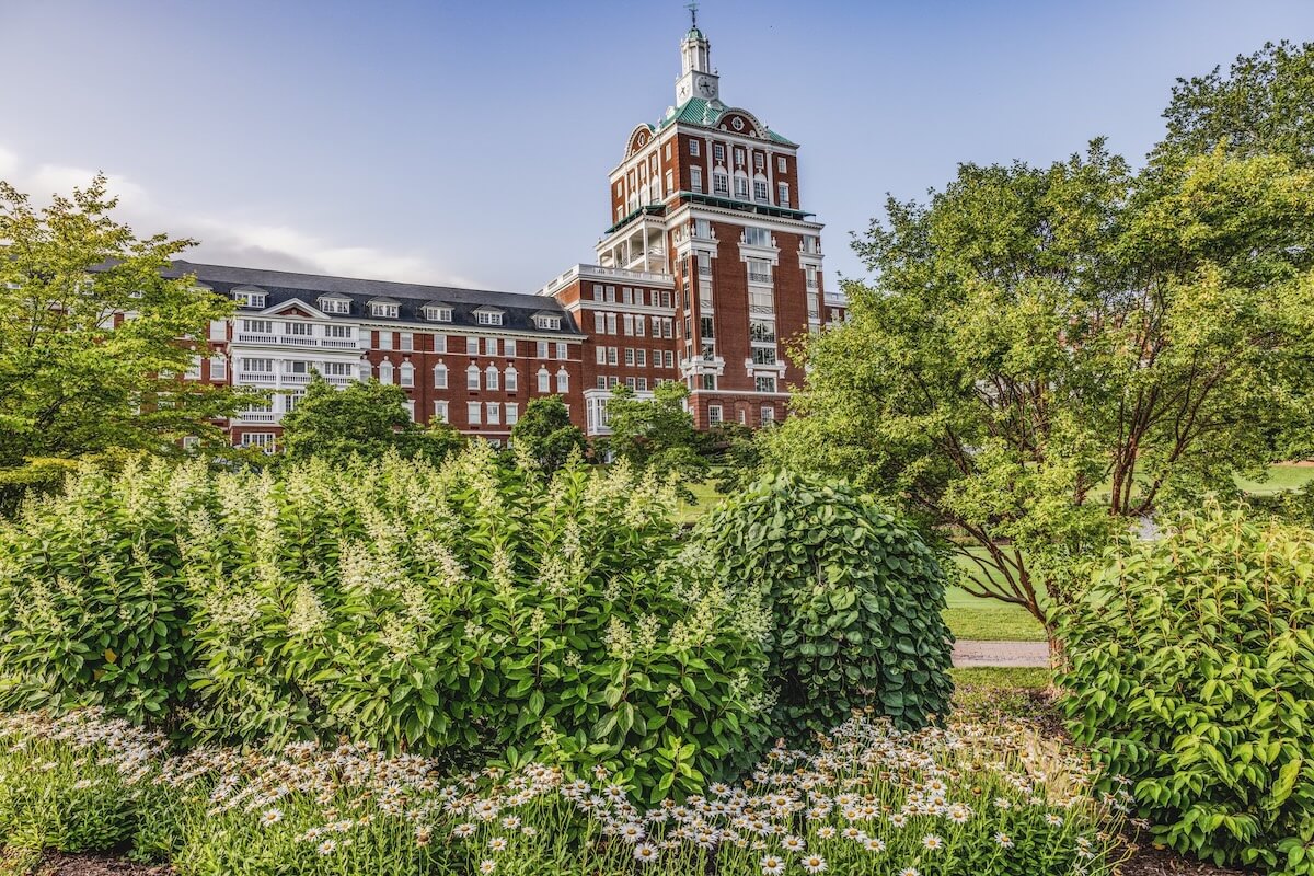 Nestled in small town Virginia, this historic red brick building with a tower stands proudly against the clear blue sky, enveloped by lush greenery and blooming flowers.