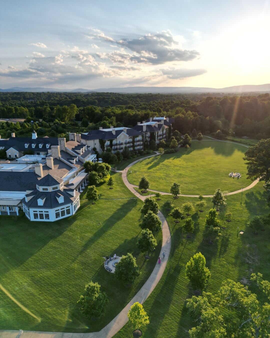 Aerial view of a large estate in small town Virginia, with several buildings surrounded by expansive green lawns and pathways. Trees and the scenic landscape stretch into the background under a partly cloudy sky.