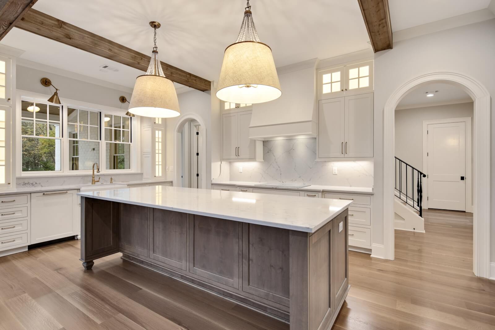 A bright kitchen featuring Magnolia Homes charm showcases wooden beams, a large island, marble countertops, pendant lights, and elegant arched doorways.