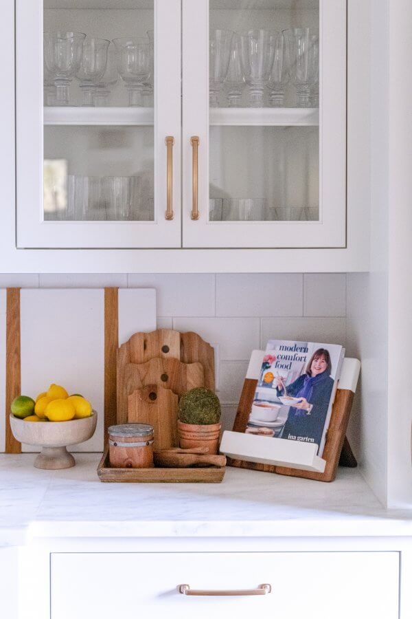 A close-up of a kitchen vignette featuring cutting board, a bowl of citrus, and a cookbook.