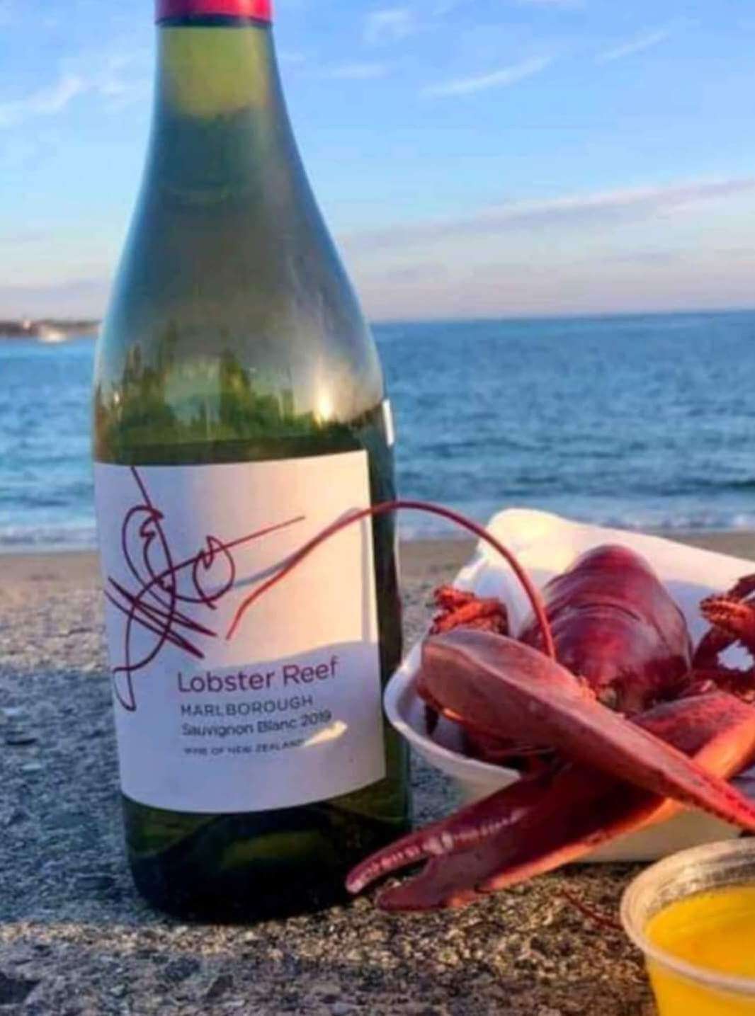 Bottle of 'lobster reef' winer on beach next to lobster dinner