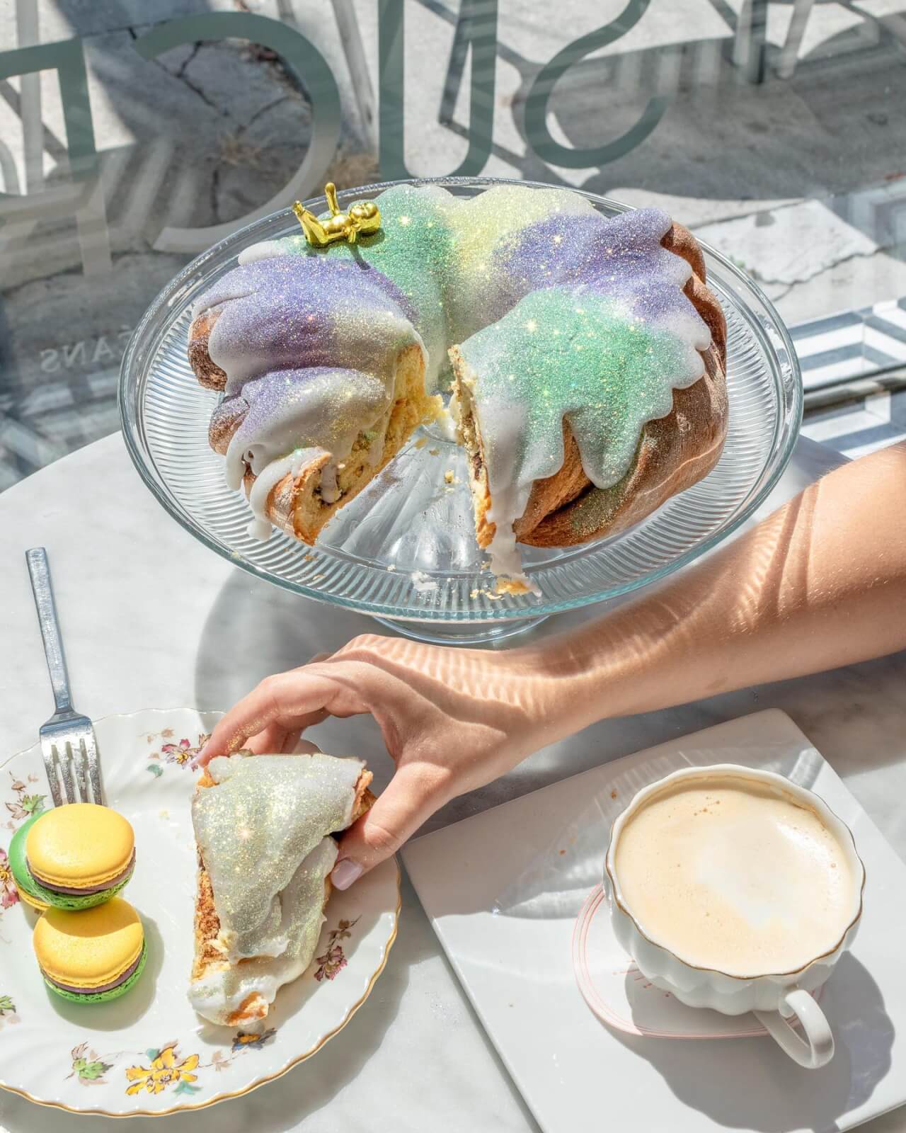 king cake on platter beside latte and plate of macarons