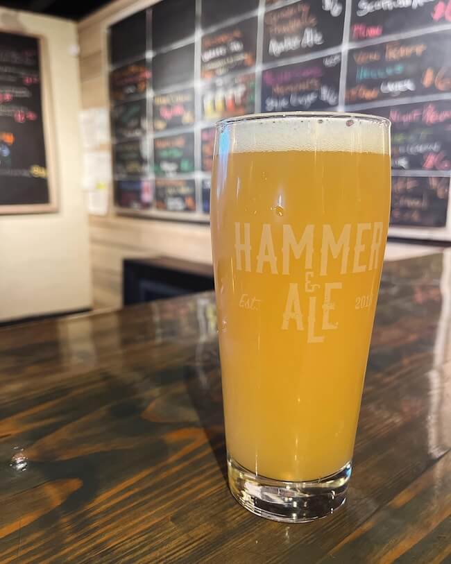 A pint of hazy beer from a local Memphis brewery on a bar table with the logo "hammer ale" printed on the glass.