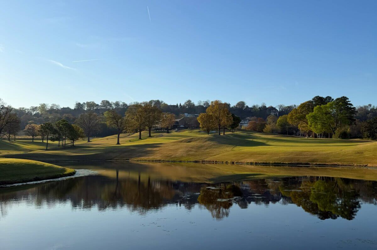 Your Guide to BHAM's Charming Highland Park Neighborhood - 3 A calm pond reflects trees and grassy hills on a Highland Park golf course under a clear blue sky, with houses visible in the distant background.