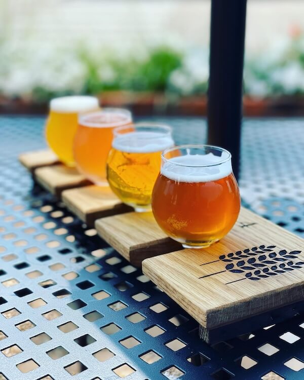 A flight of four craft beers from local Memphis breweries served on a wooden paddle, arranged on a metal table.