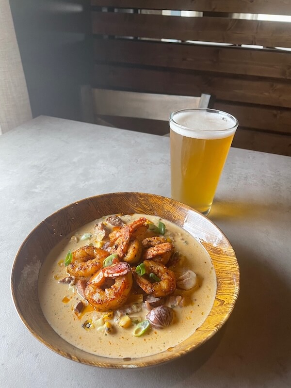 A plate of seasoned shrimp with sauce accompanied by a glass of beer from Memphis breweries on a wooden table.