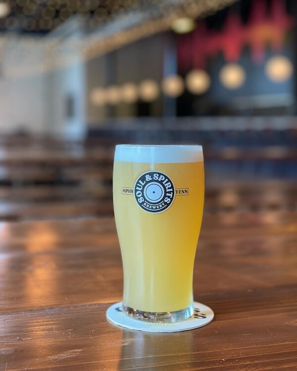 A glass of beer from Memphis Breweries on a wooden bar countertop with the brewery's coaster underneath.