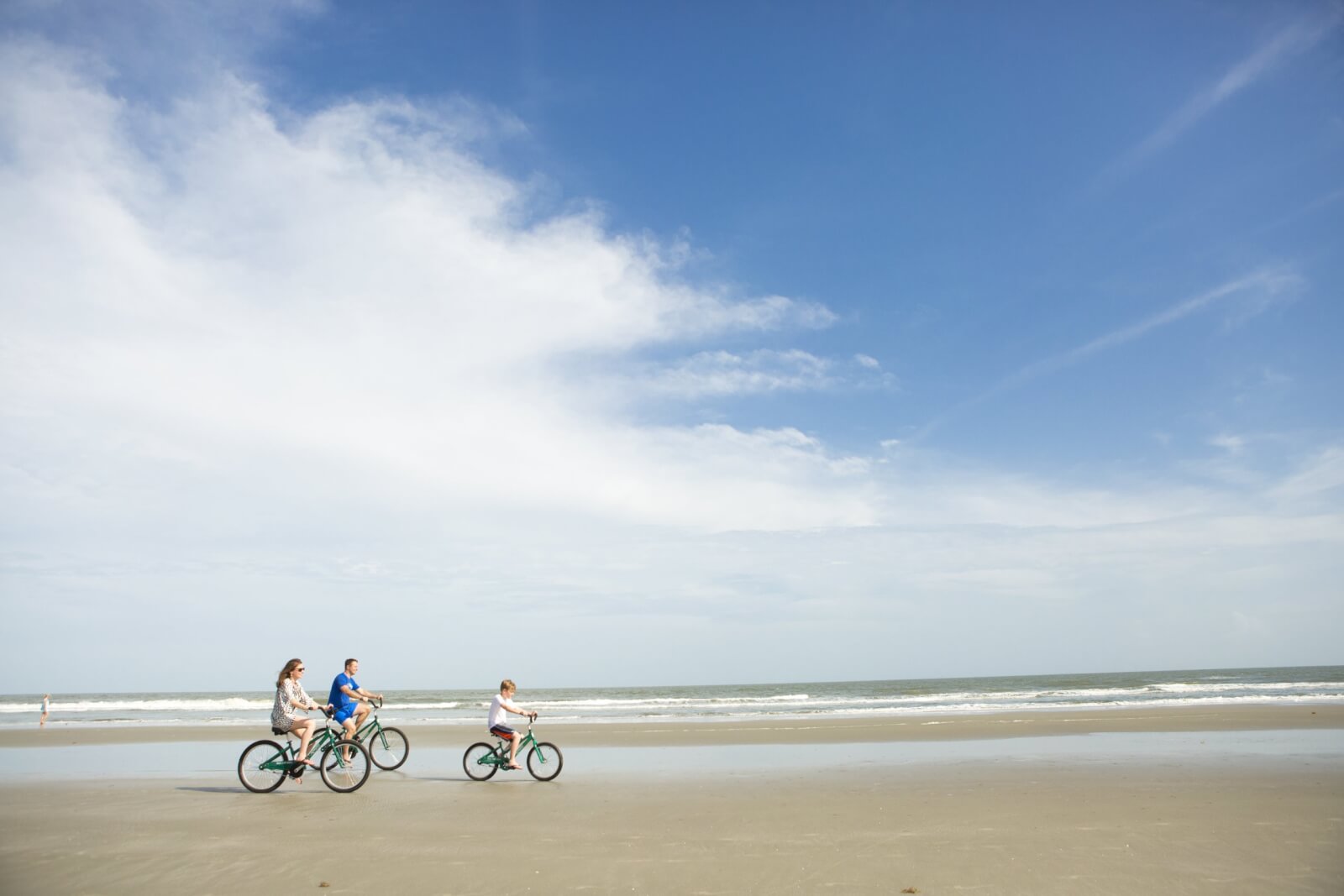 Family of three biking on sandy beach at Kiawah Island Golf Resort