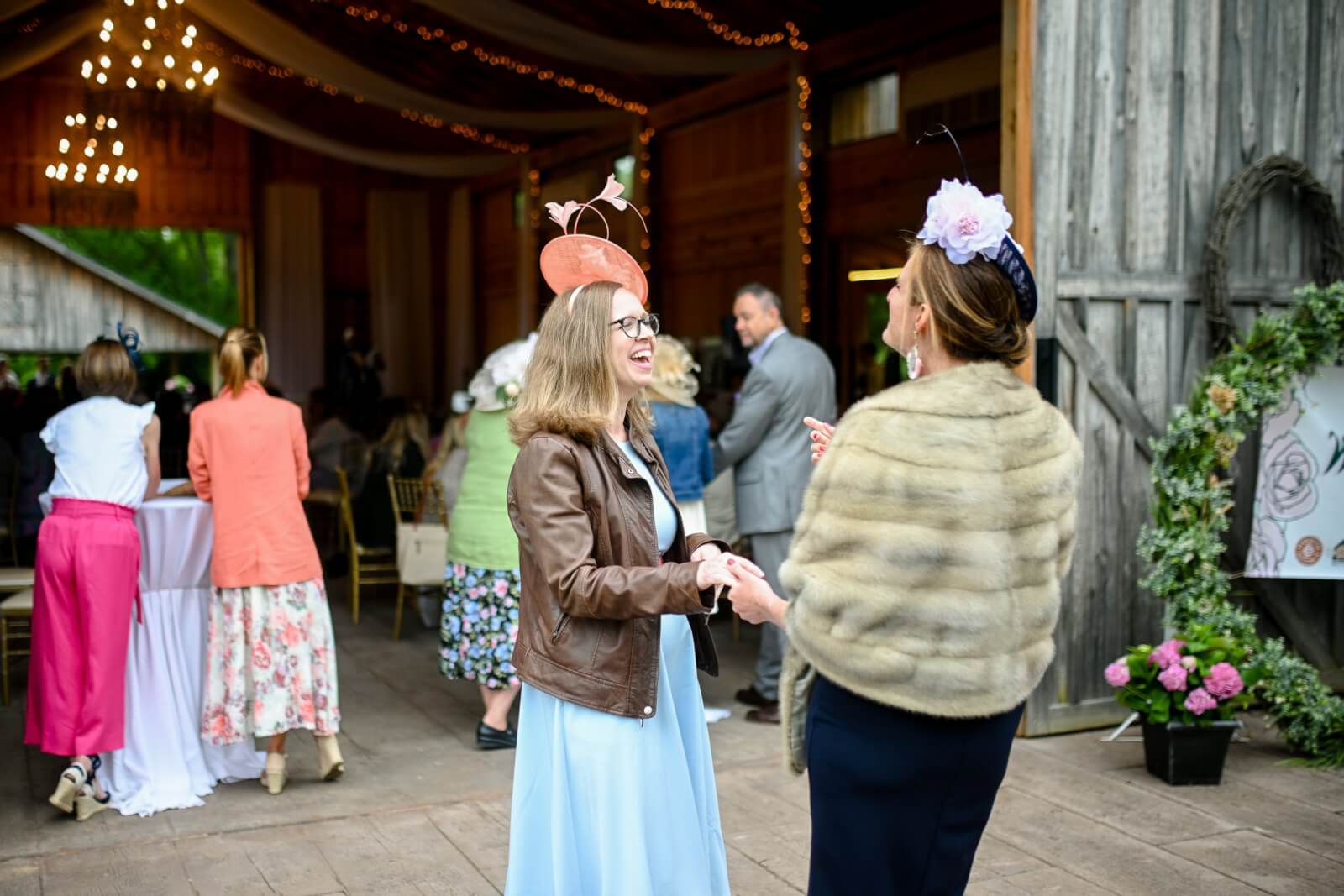 Two women laughing at a Derby-themed fundraiser.