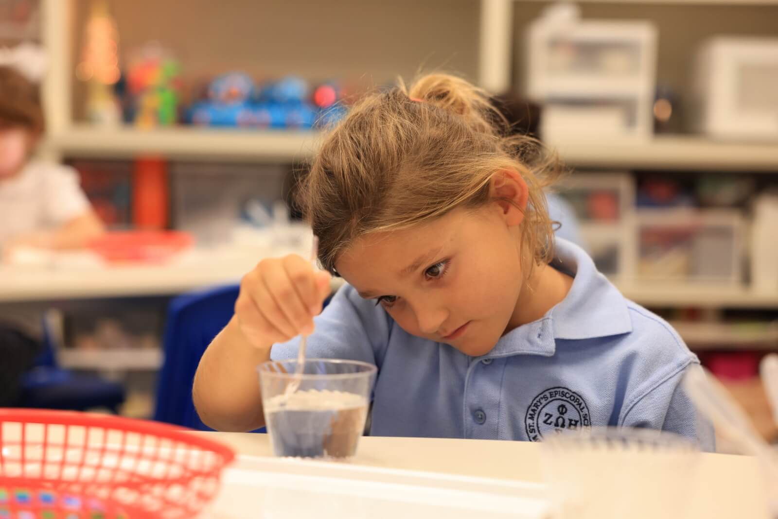Young girl in blue polo shirt swirling a spoon in a cup of water
