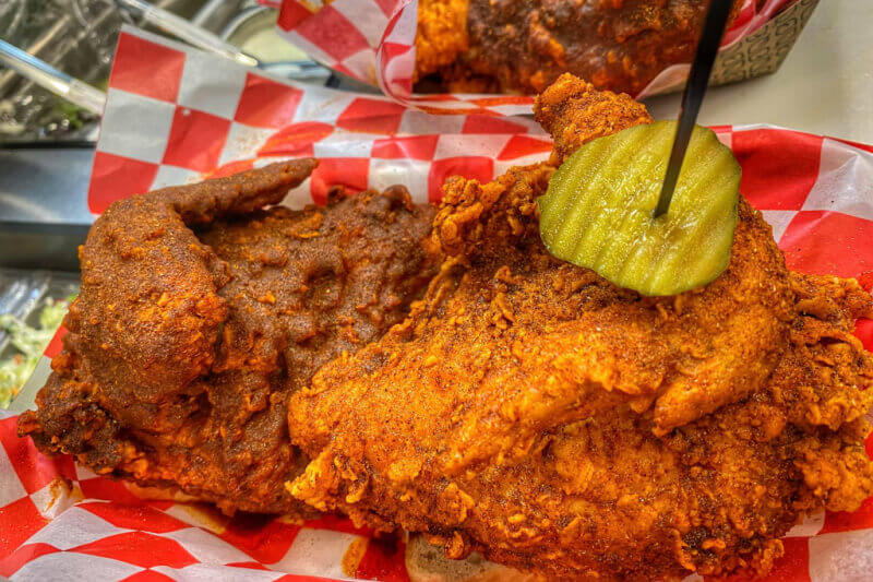 Two pieces of spicy fried chicken served on red and white checkered paper, topped with sliced pickles—a must-try at top BNA restaurants and Nashville airport restaurants.