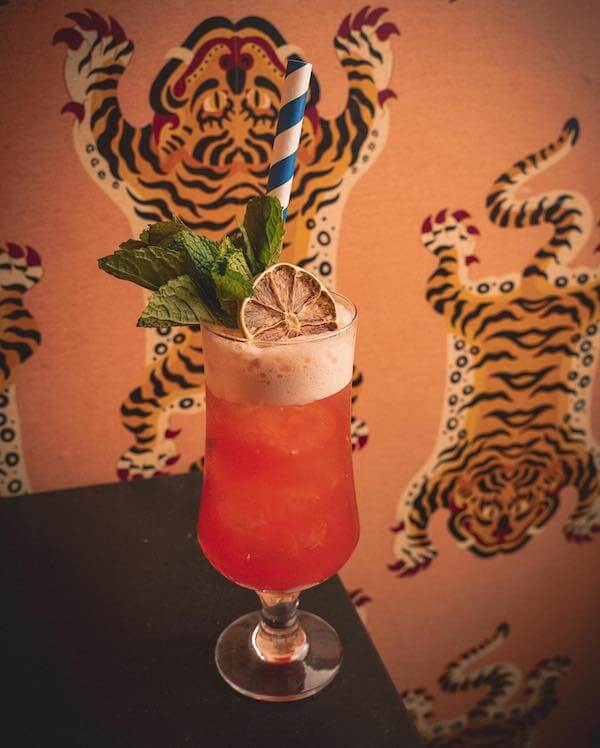 pink tropical cocktail with straw in front of tiger wallpaper